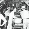 The man in the center of the photo with a hat, white shirt and a tie is Riley Maness. He's inspecting tomatoes brought into his shed at the corner of Main and Second Street in Rusk. Another shed owned by J.P. Acker was located at the other end of Second Street. Both sheds were adjacent to the railroad.