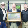 Artist Raymond Ryan (left) and Angelina County Constable Trey Trevathan (right) presented Judge Chris Davis with a print of the Maydelle General Store that Mr. Ryan painted while working in the area.