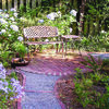 A gray pea gravel path edged with bricks leads to a quiet garden spot. Blue hydrangeas and Lily of the Nile brighten the area.